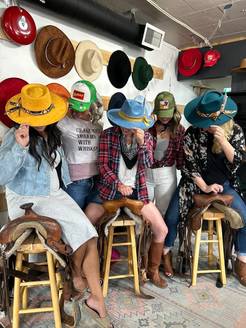 Guests playfully hiding behind their custom styled hats, seated on saddle stools