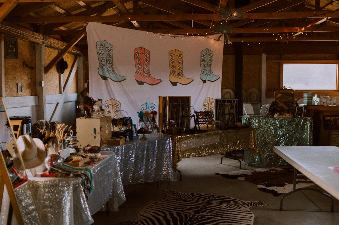 Hat bar setup inside a barn venue with a hand-painted boot banner
