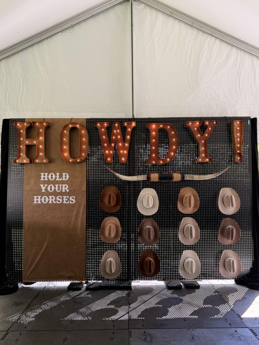 HOWDY! Hold your horses — marquee sign above a wall of custom cowboy hats