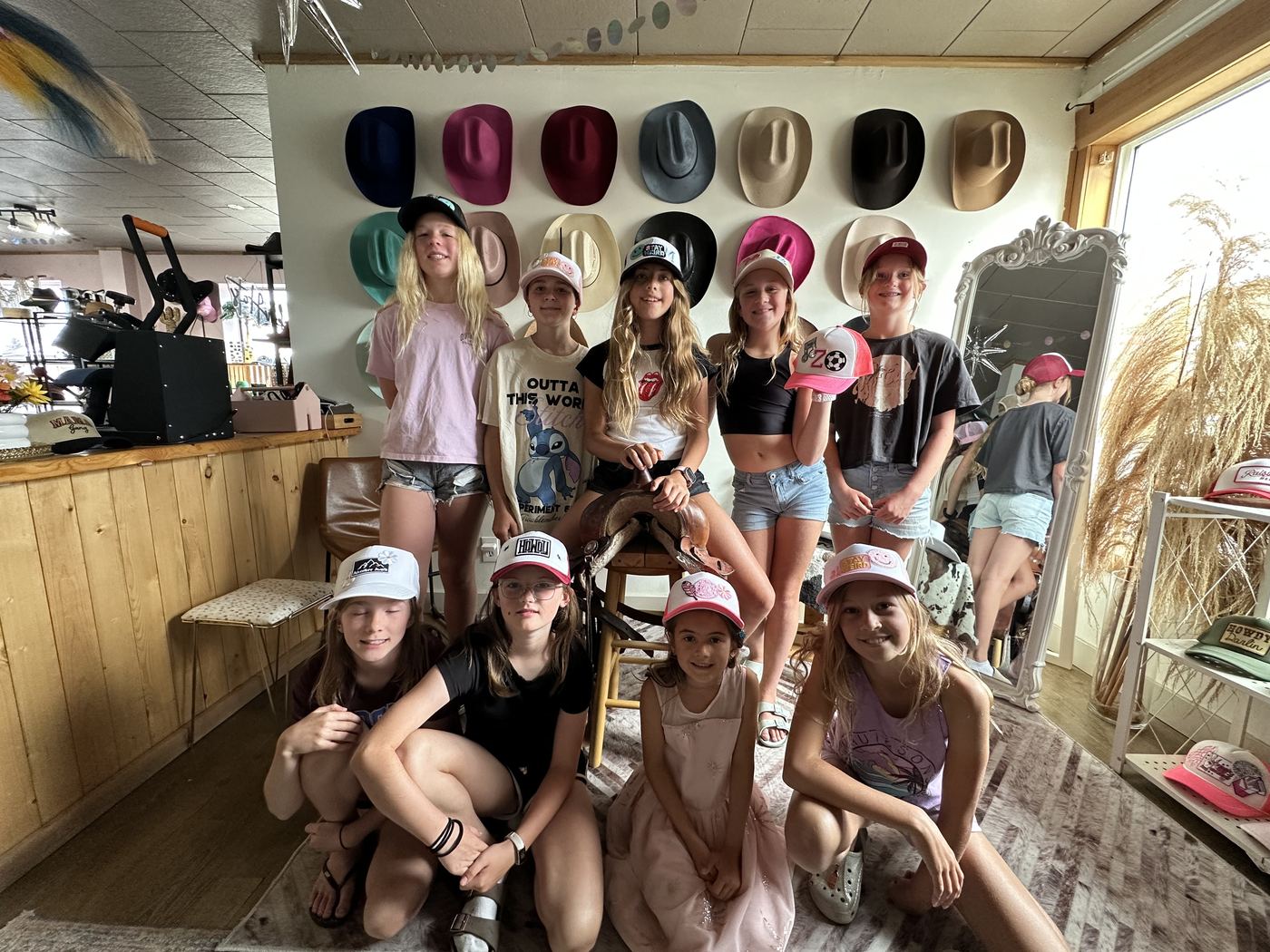 Group of kids posing with custom trucker hats in front of the hat wall at Saddle N Spurs