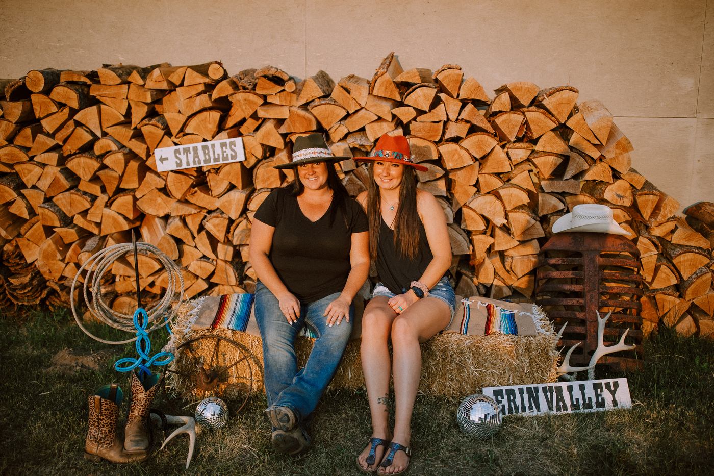 Two guests posing by the Erin Valley stables sign with disco balls and hay bales