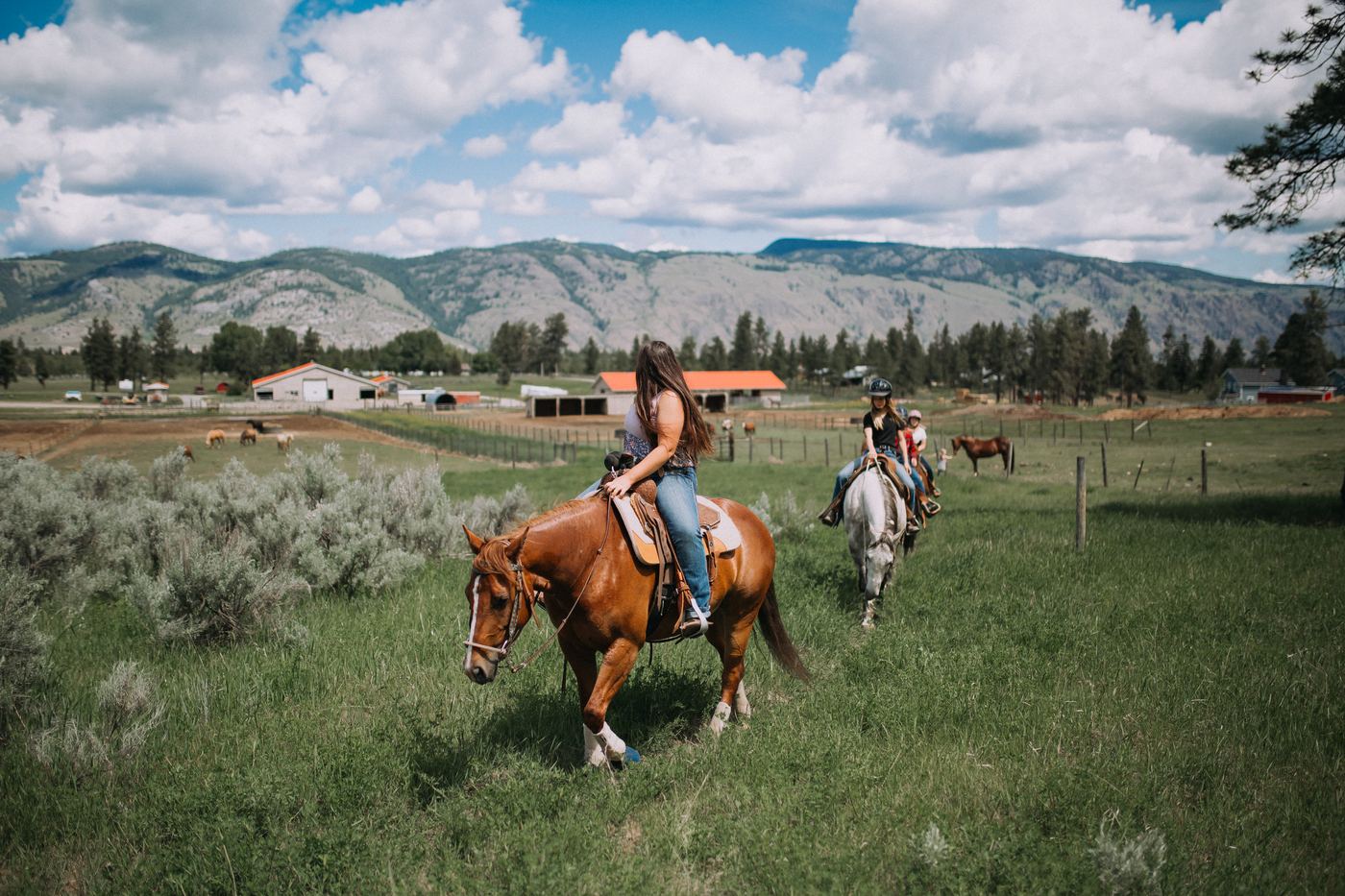 Riders on horseback with the Erin Valley Riding Stables ranch buildings and mountains in the background