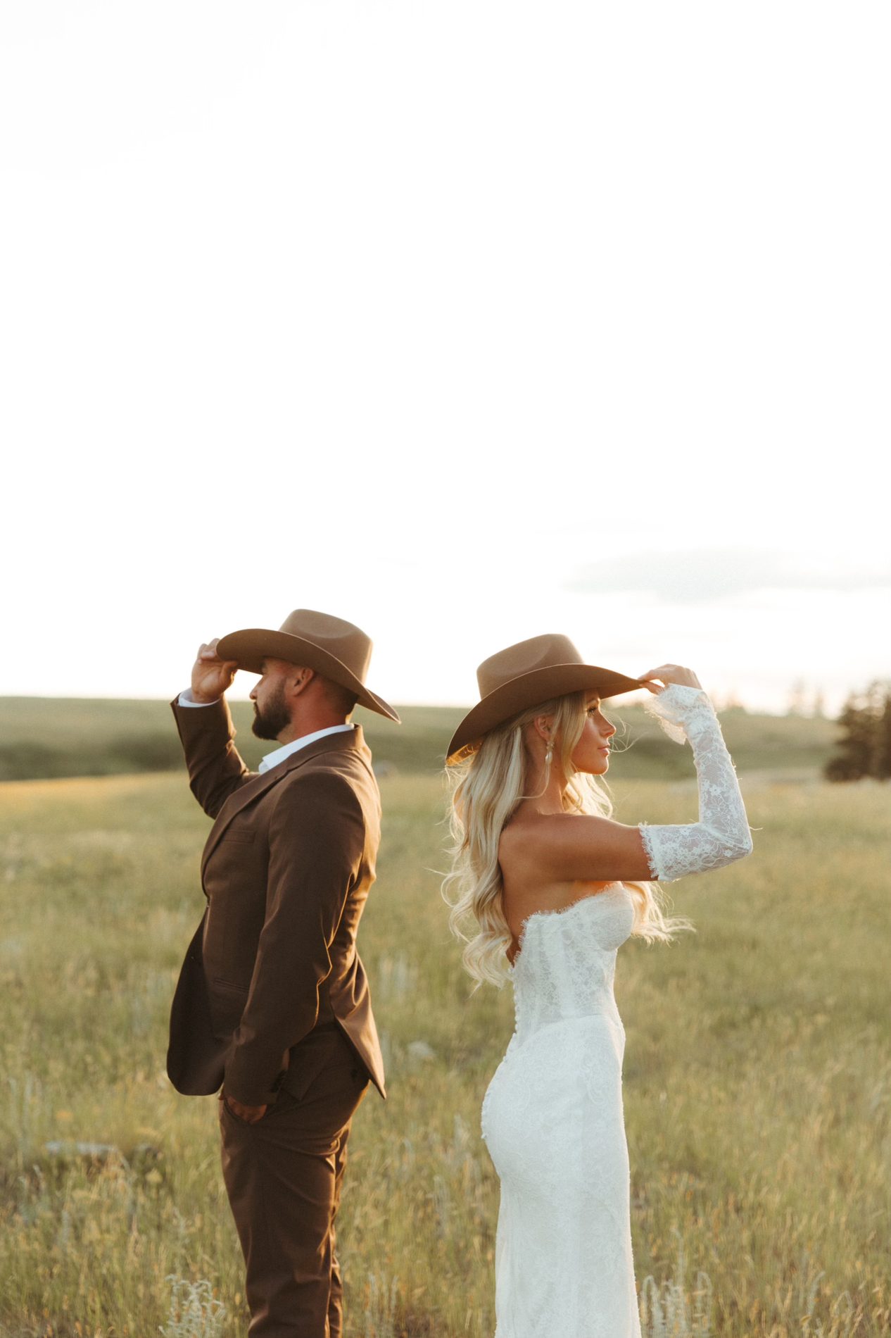 Bride and groom holding the brims of their brown cowboy hats in a golden field