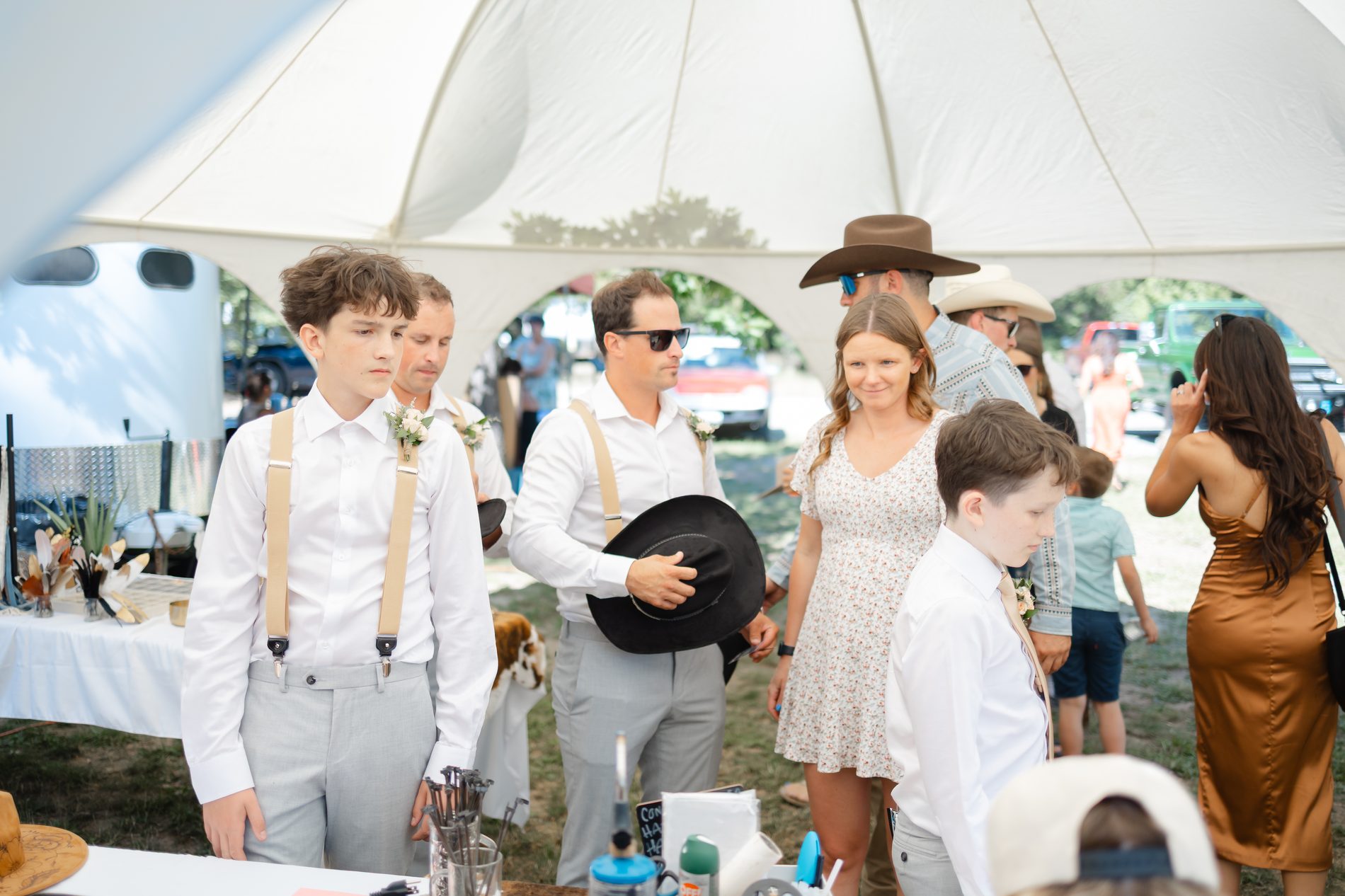 Groomsmen in suspenders holding their black cowboy hats under the reception tent