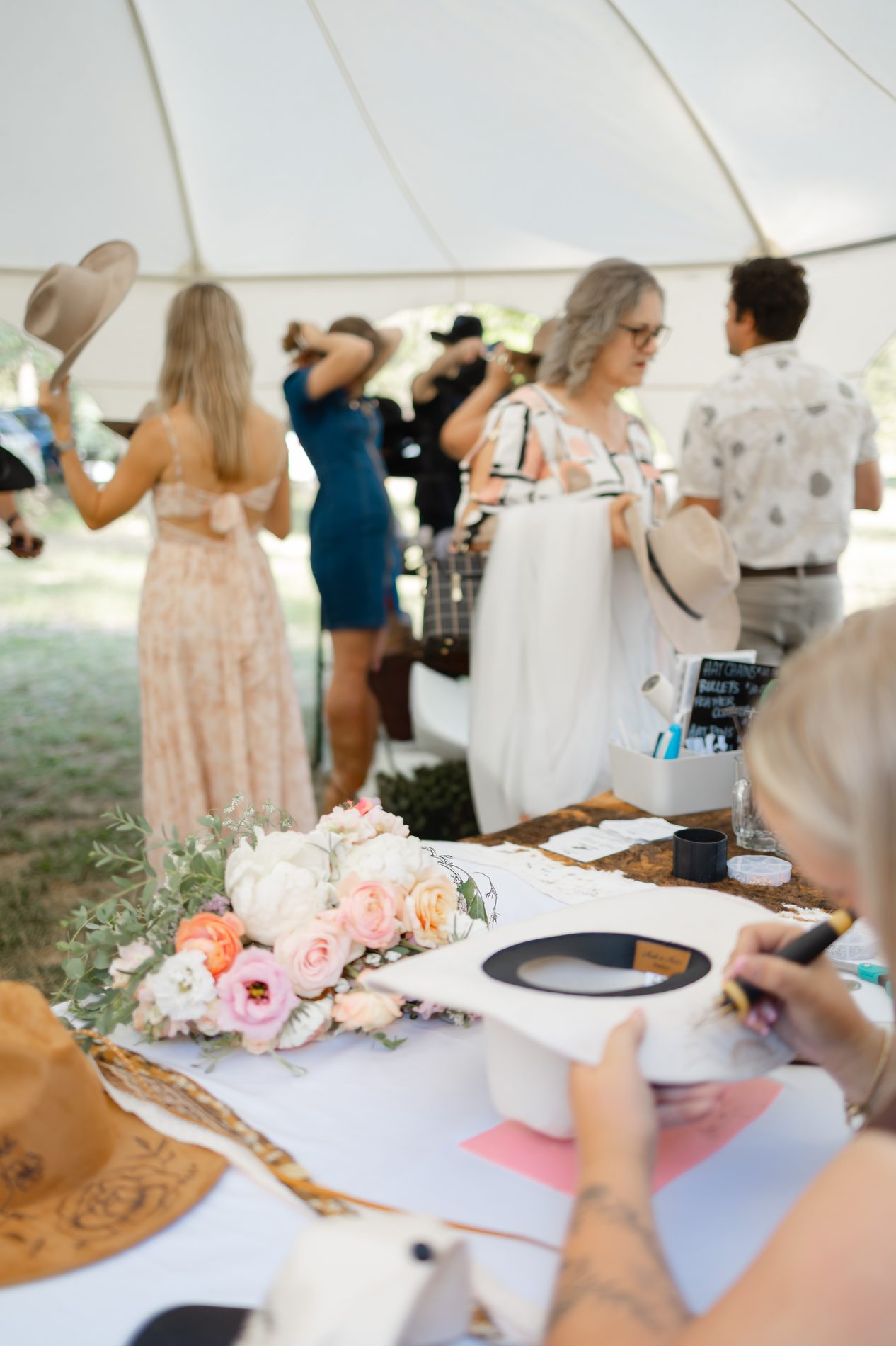 Hat bar signing table decorated with peach roses and peonies at a wedding reception